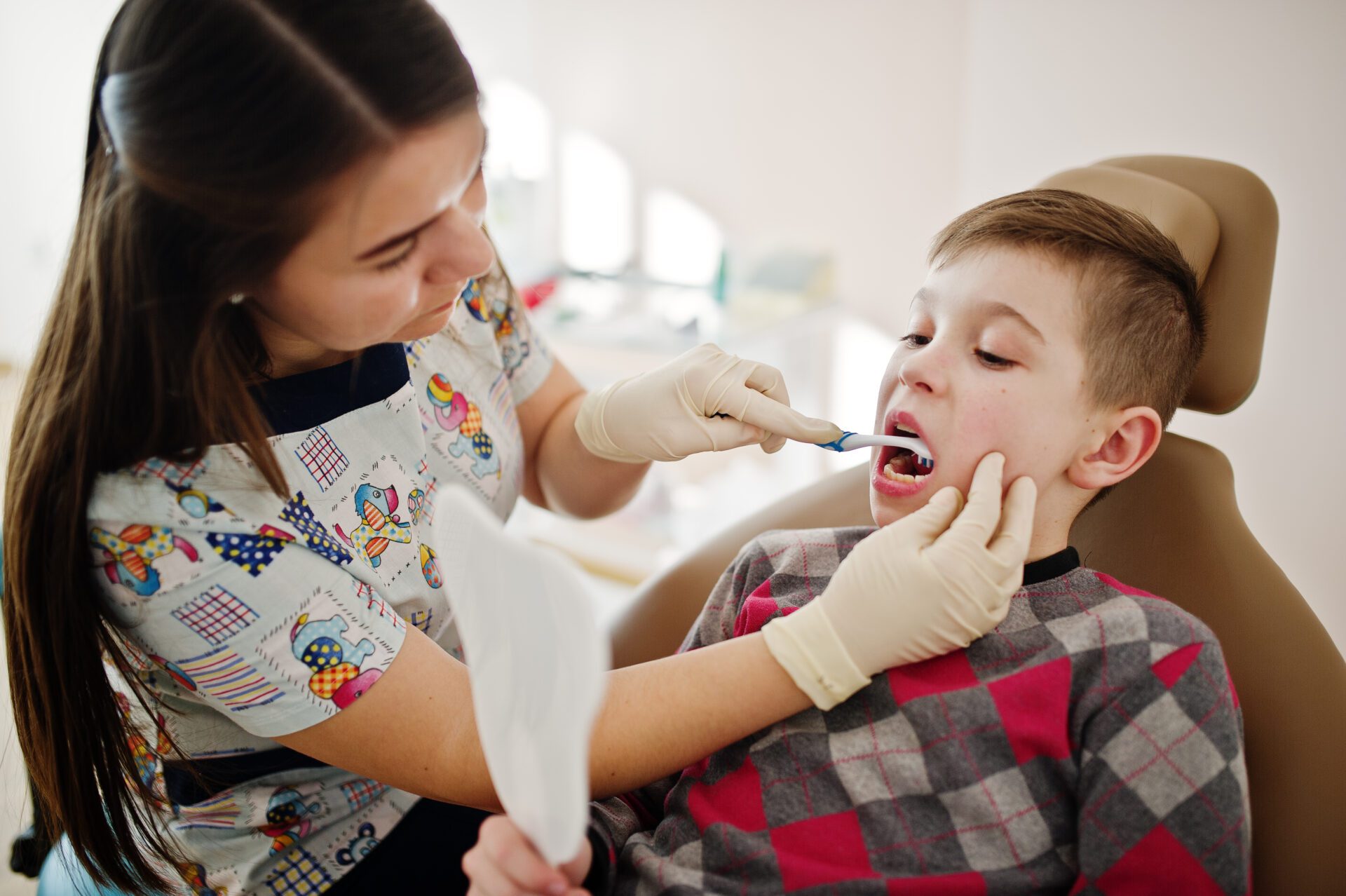 Little boy sitting on dentist chair getting a treatment after injury from female dentist. 